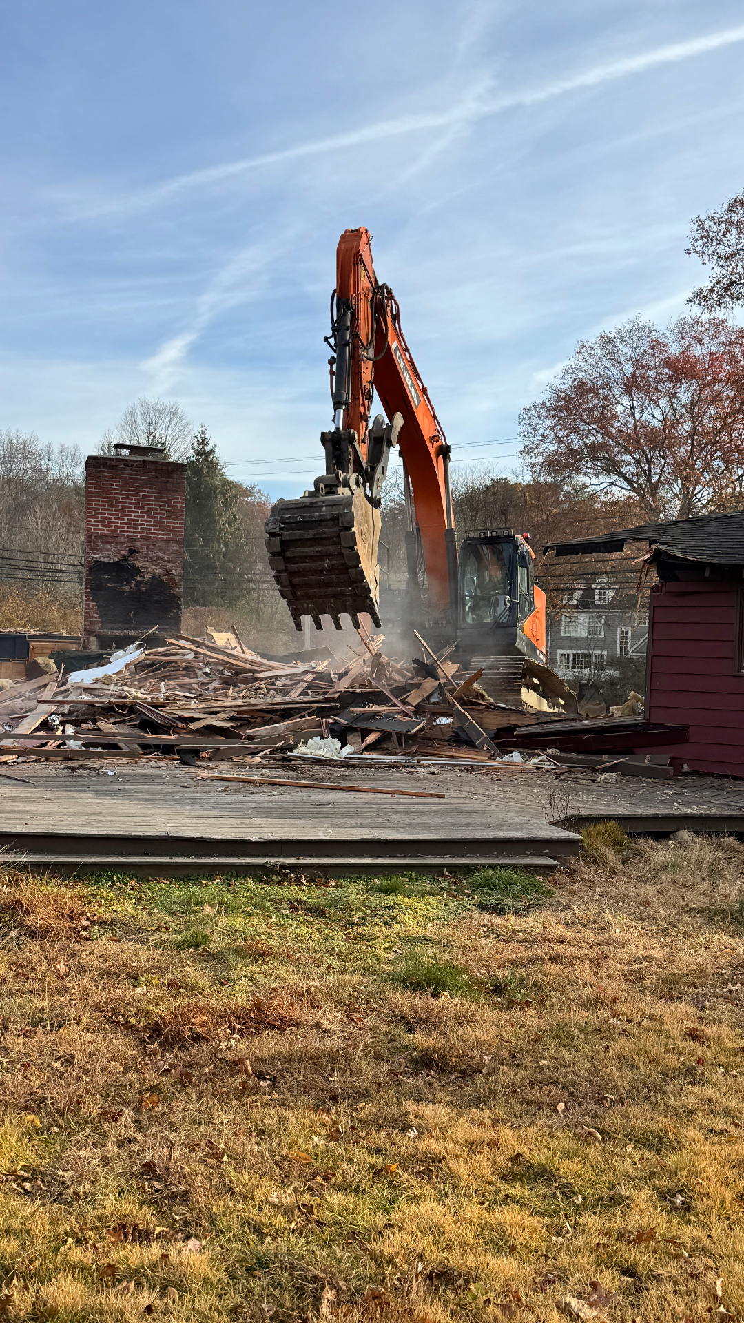 Excavator breaking down remaining framing and debris beside the original brick chimney.