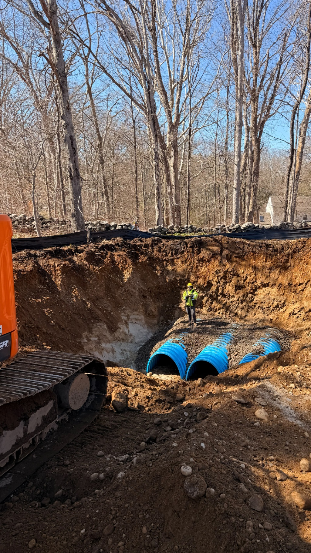 Site supervisor inspecting a stormwater infiltration system of blue chambers set in gravel within a deep excavation.