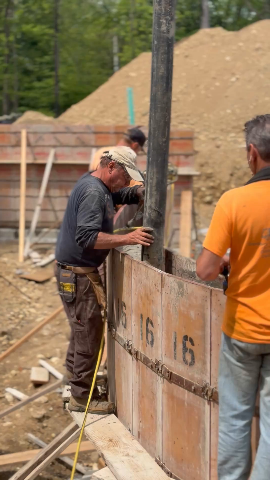 Crew guiding a concrete pump hose into wall formwork during a foundation pour.