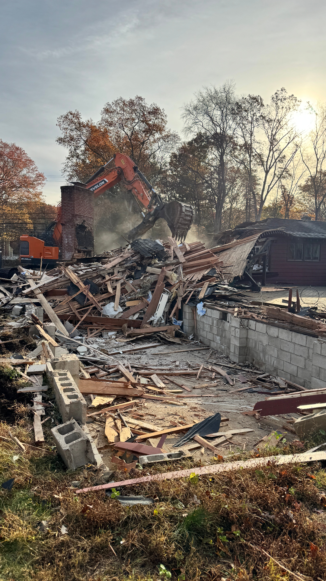 Excavator demolishing an existing residence at sunrise, clearing the site for new construction.