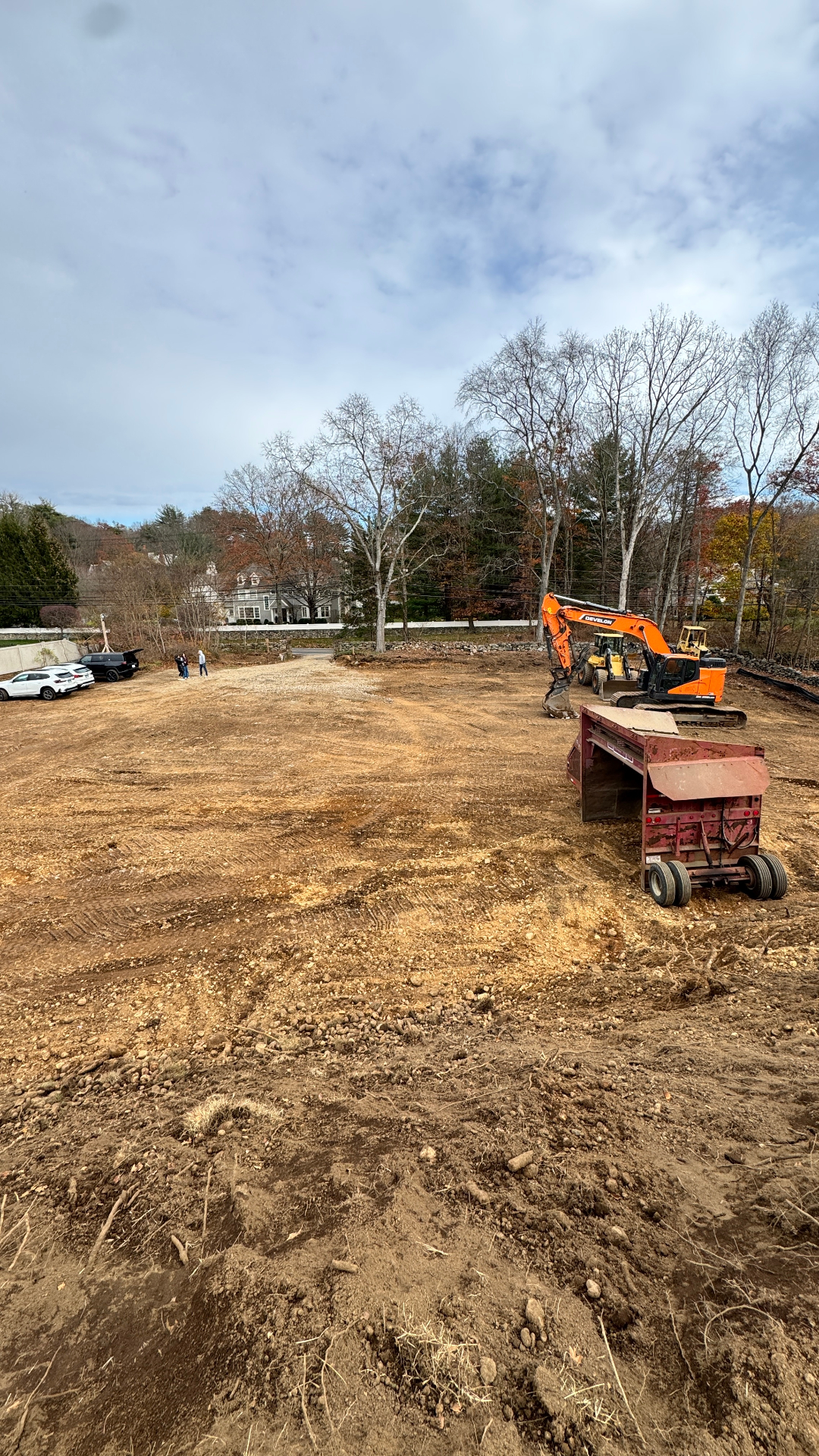 Cleared and graded building site with excavator and material spreader ready for foundation work.