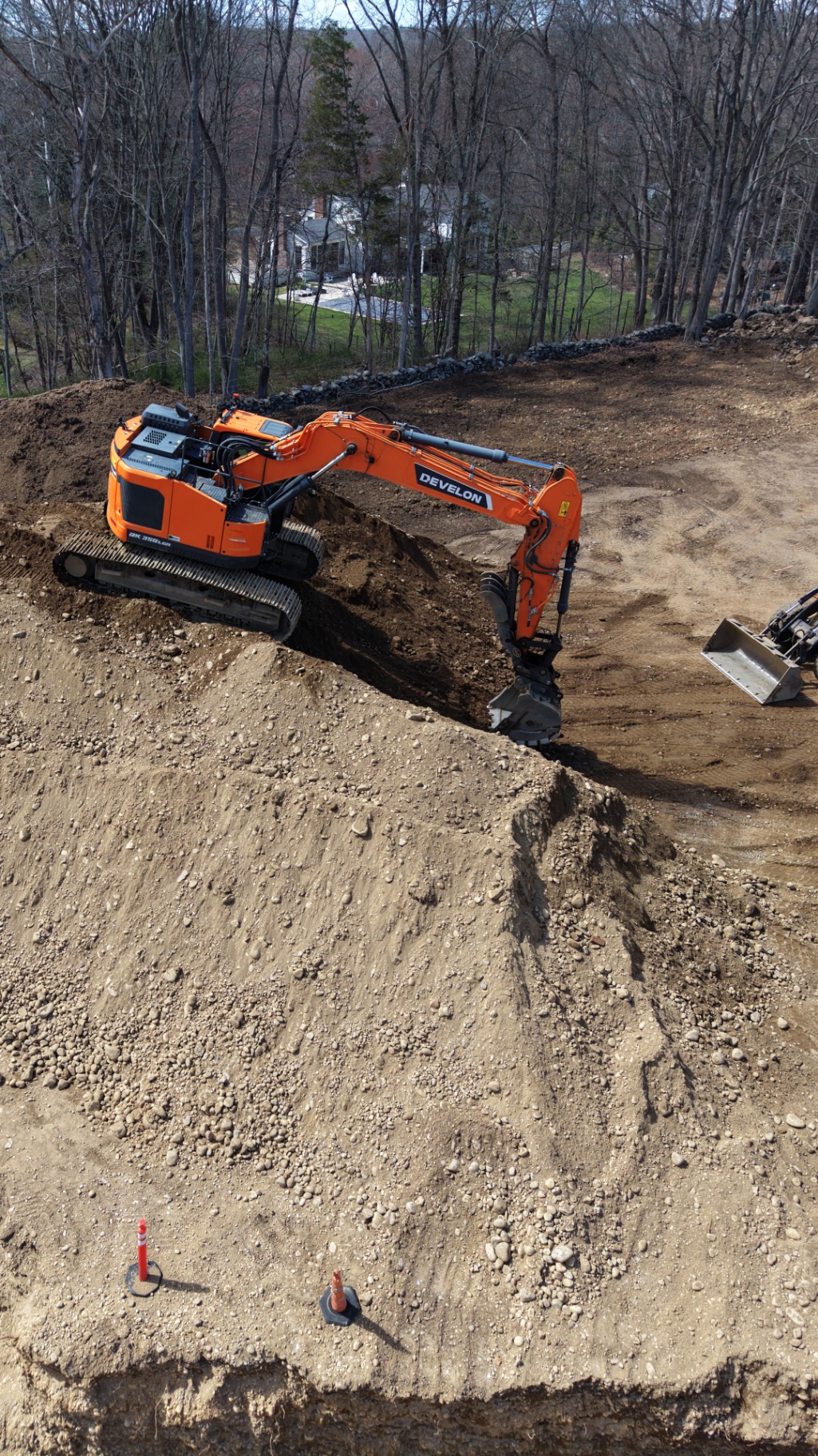 Aerial view of an excavator cutting into a hillside during site excavation on a wooded lot.