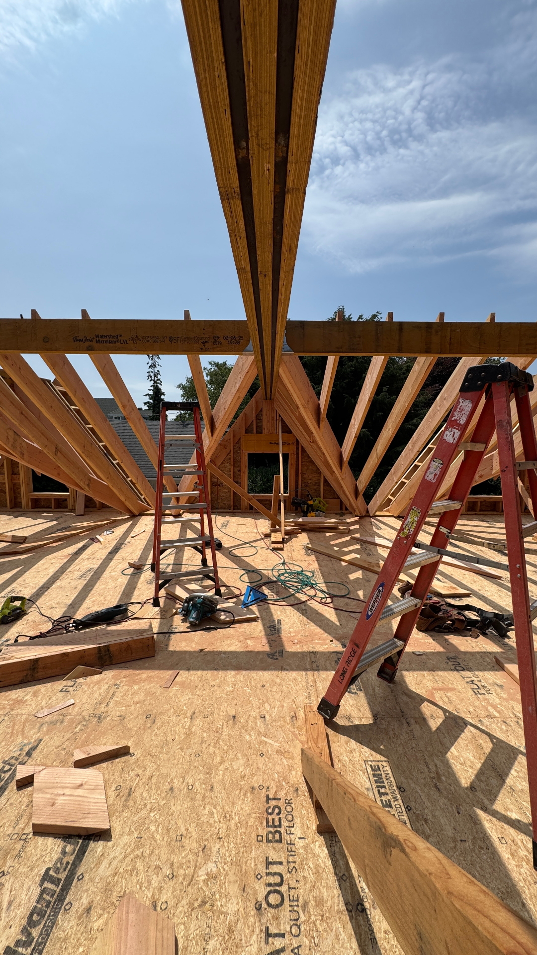 Interior view of exposed roof rafters and ridge beam framing against a bright sky, showing the structural skeleton of a new home.
